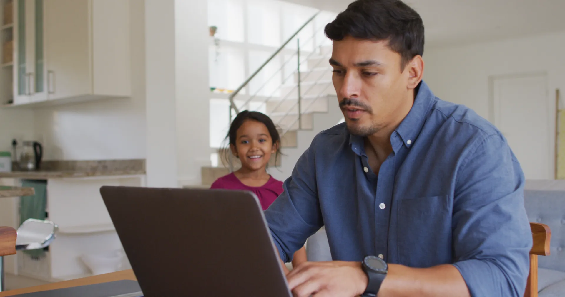 Un padre trabaja en su computador mientras su hija lo acompaña.